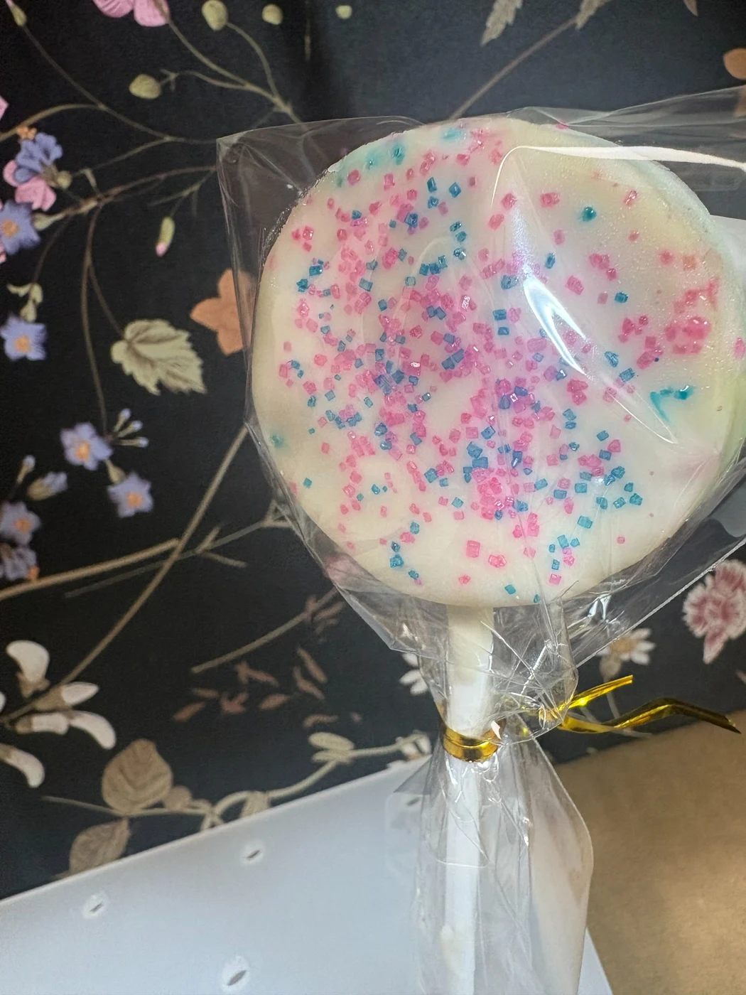 A wrapped white round treat topped with pink and blue sprinkles.